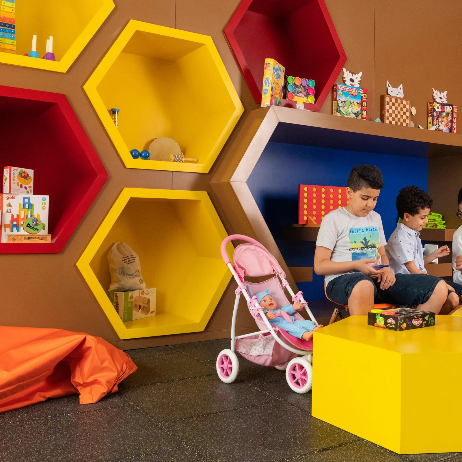 Une femme et deux enfants jouent dans une pièce colorée remplie de jouets et de livres