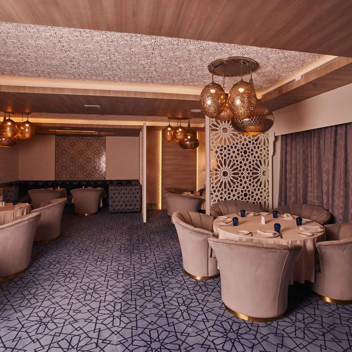 Salle de restaurant élégante avec des tables rondes, des chaises rembourrées en velours rose et des luminaires suspendus