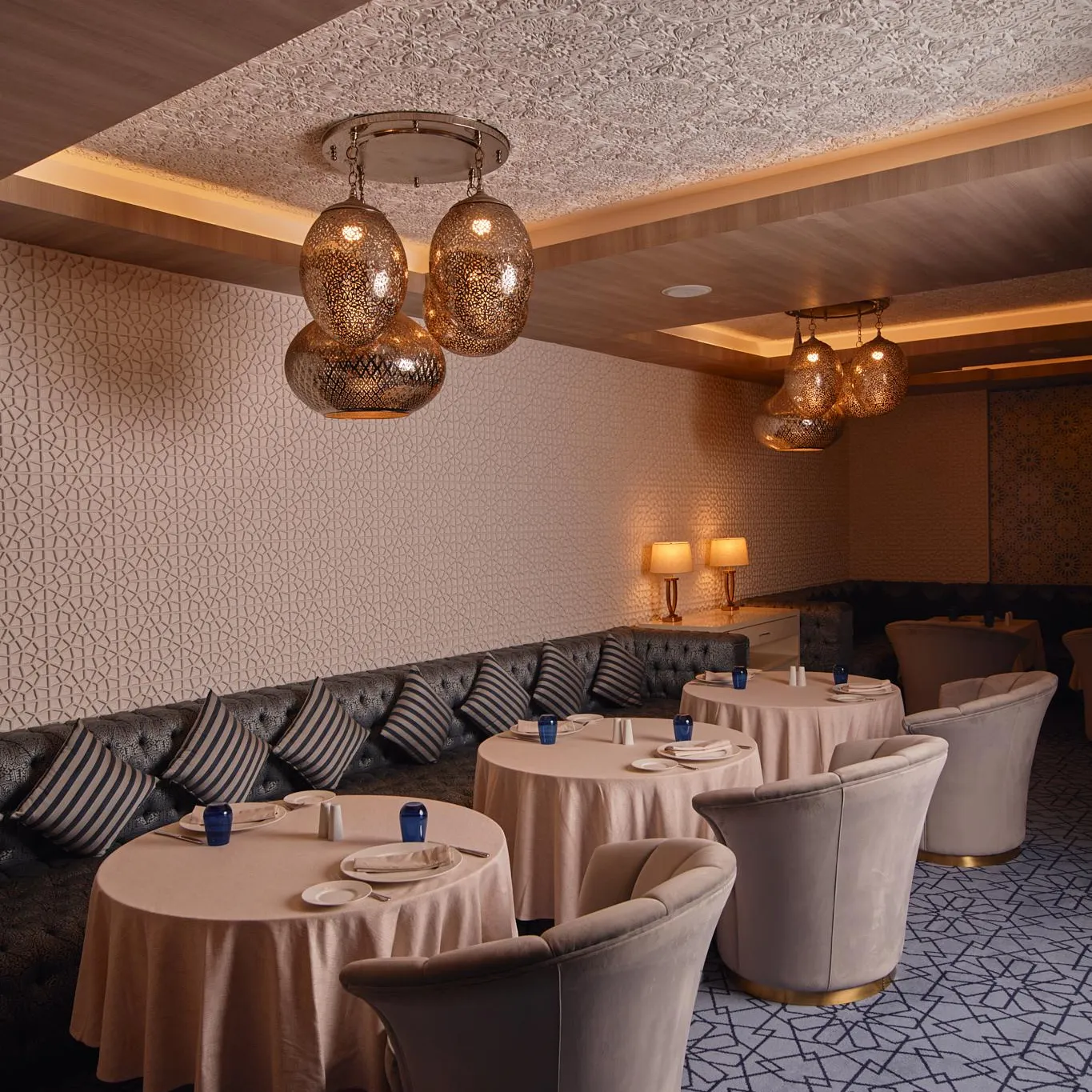 Salle de restaurant élégante avec tables rondes, chaises rembourrées et luminaires suspendus