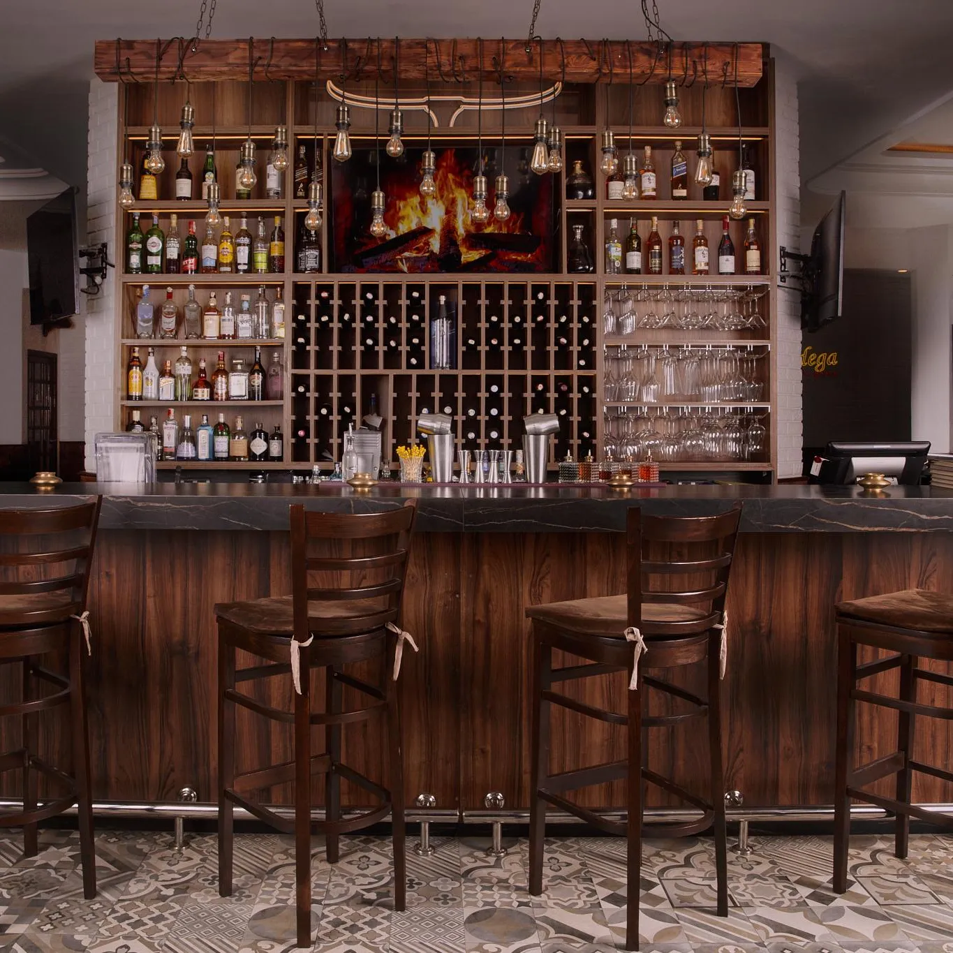 Un bar en bois avec des tabourets alignés devant, des étagères remplies de bouteilles et de verres, et un sol à motifs géométriques