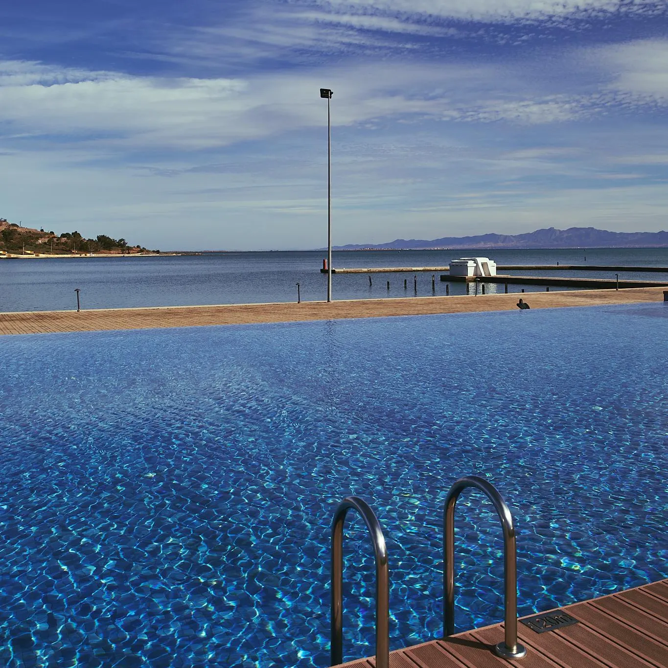 Piscine à débordement avec vue sur la mer et des montagnes au loin sous un ciel partiellement nuageux