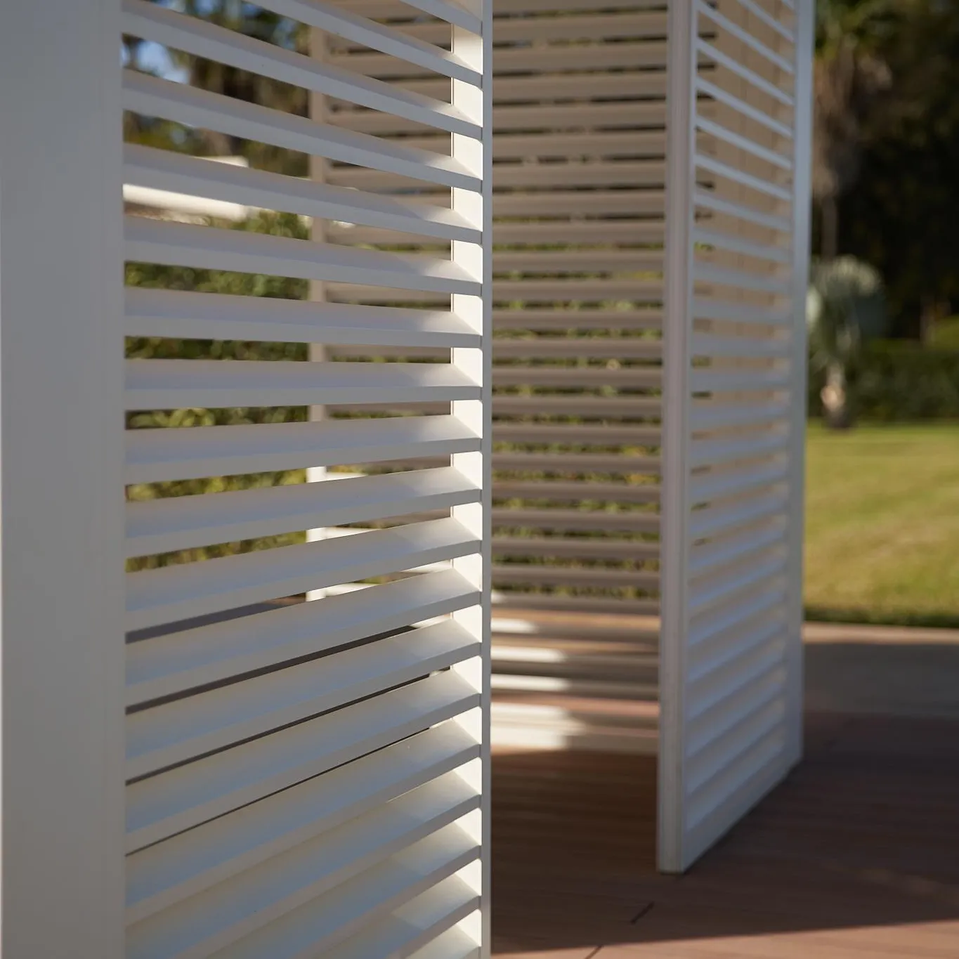 Persiennes blanches sur un balcon en bois avec vue sur un jardin et des arbres en arrière-plan