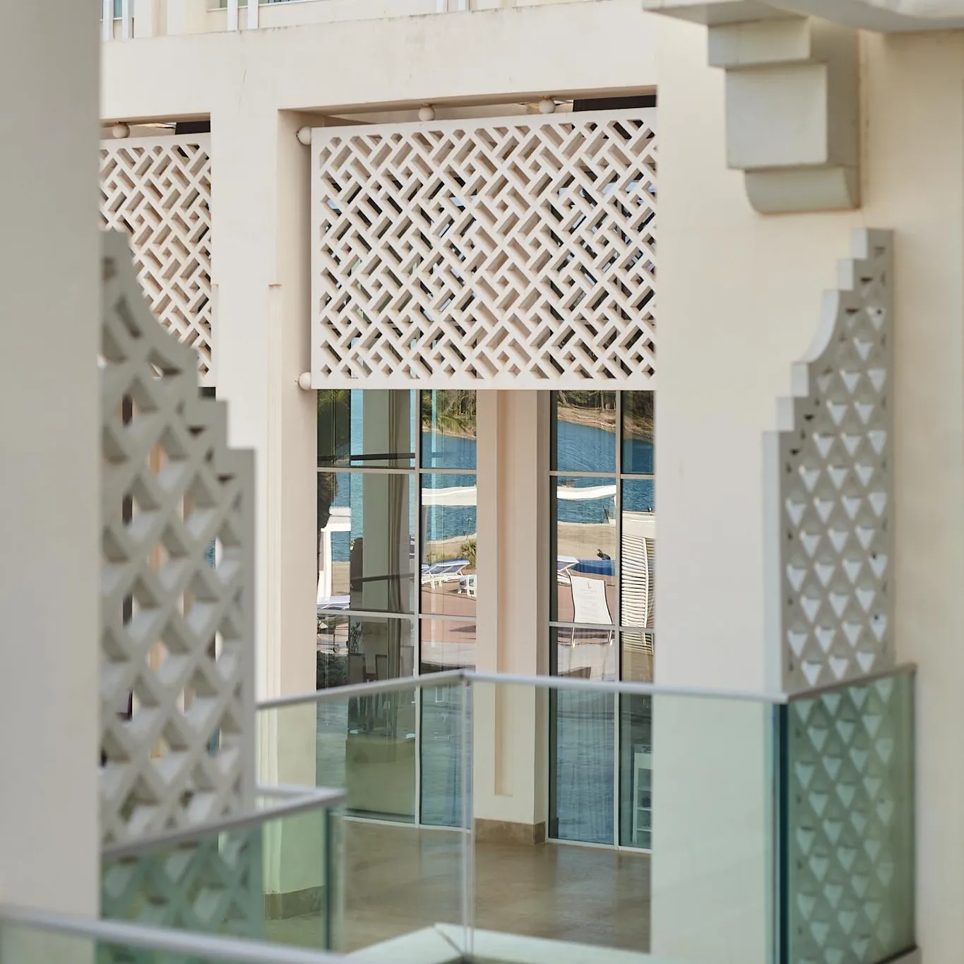 Balcon avec garde-corps en verre et panneaux décoratifs à motifs géométriques, vue sur une plage et la mer au loin