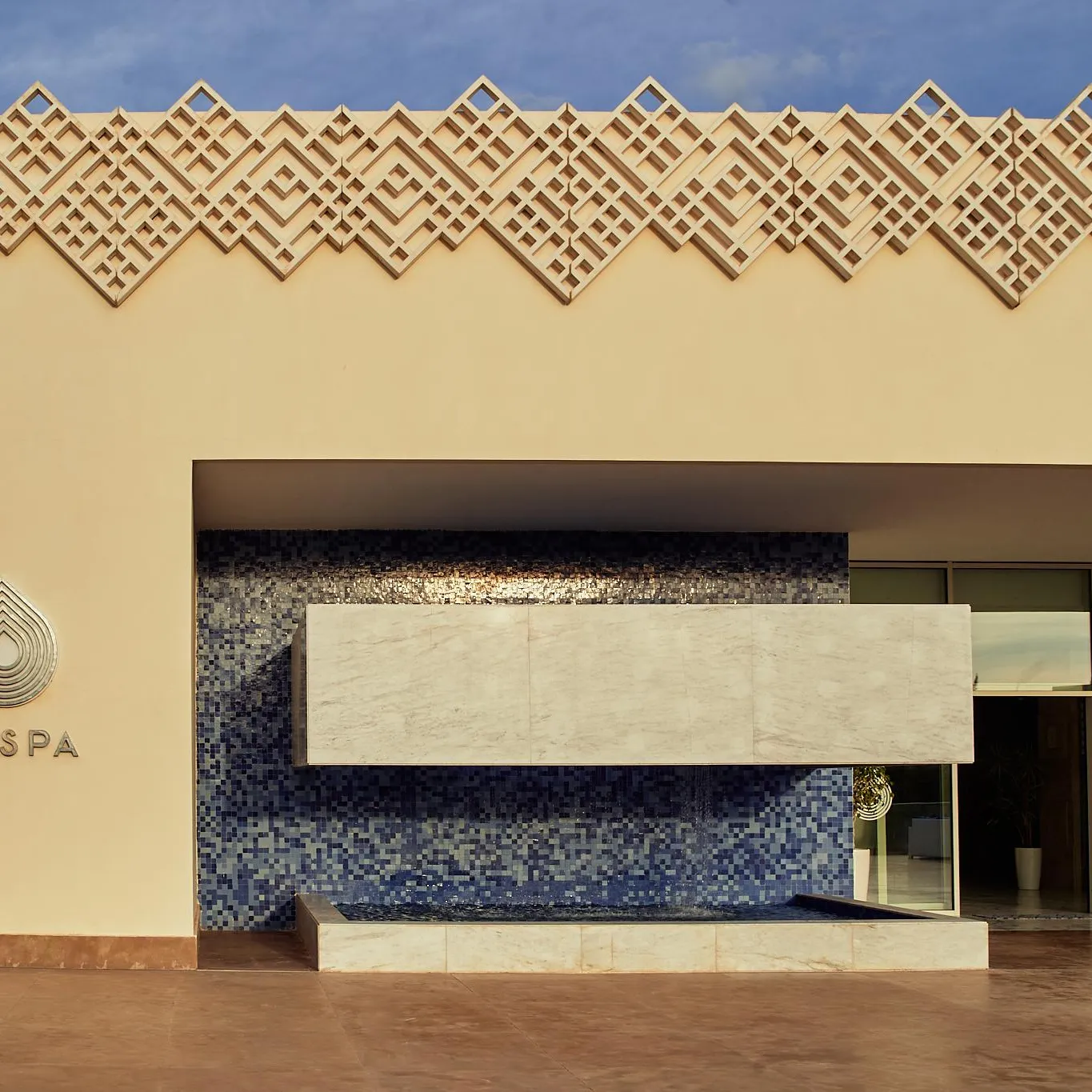 Façade d'un spa avec un mur en mosaïque bleue, une table en pierre et des plantes en pot