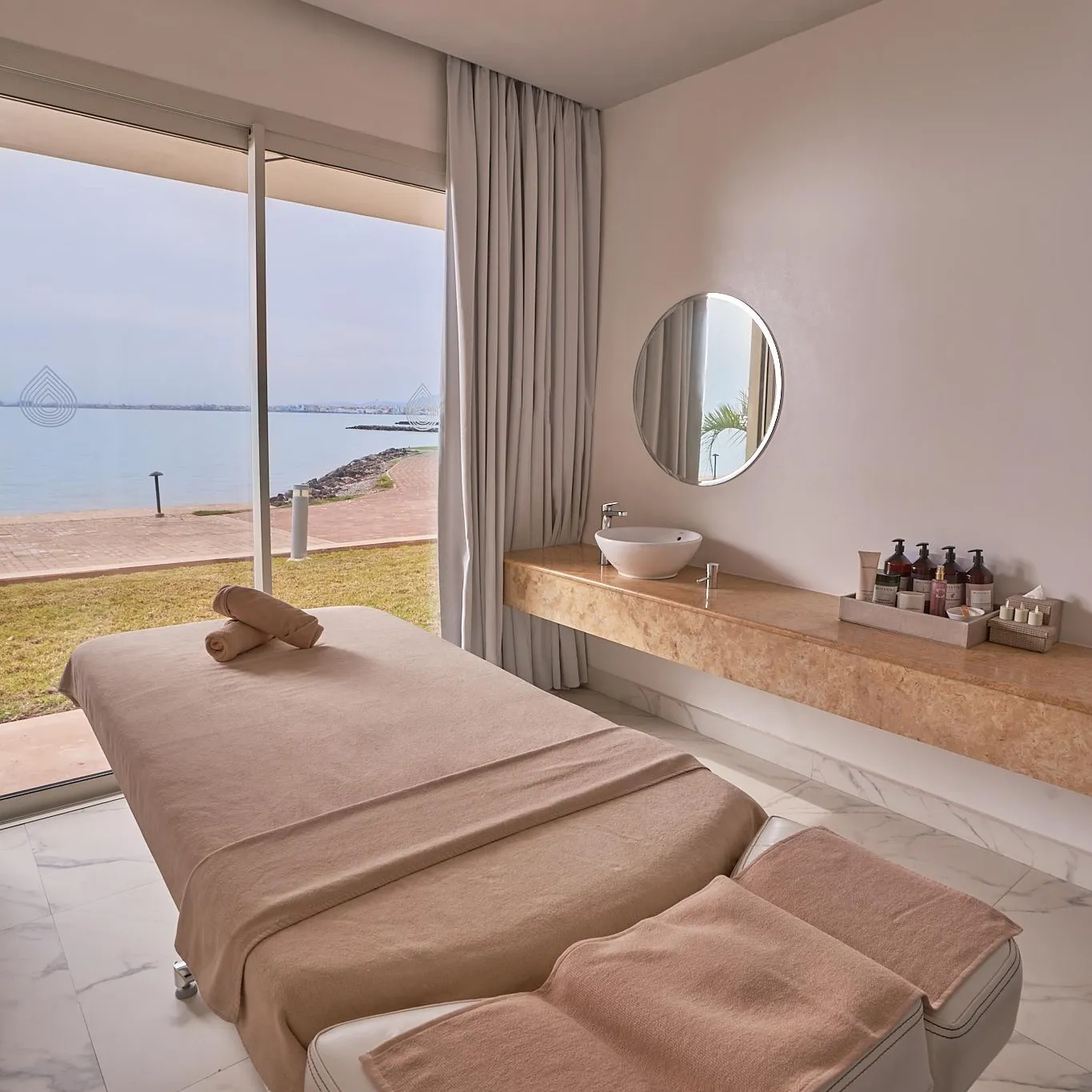 Salle de massage avec deux tables de soins, une vasque et une vue sur la mer
