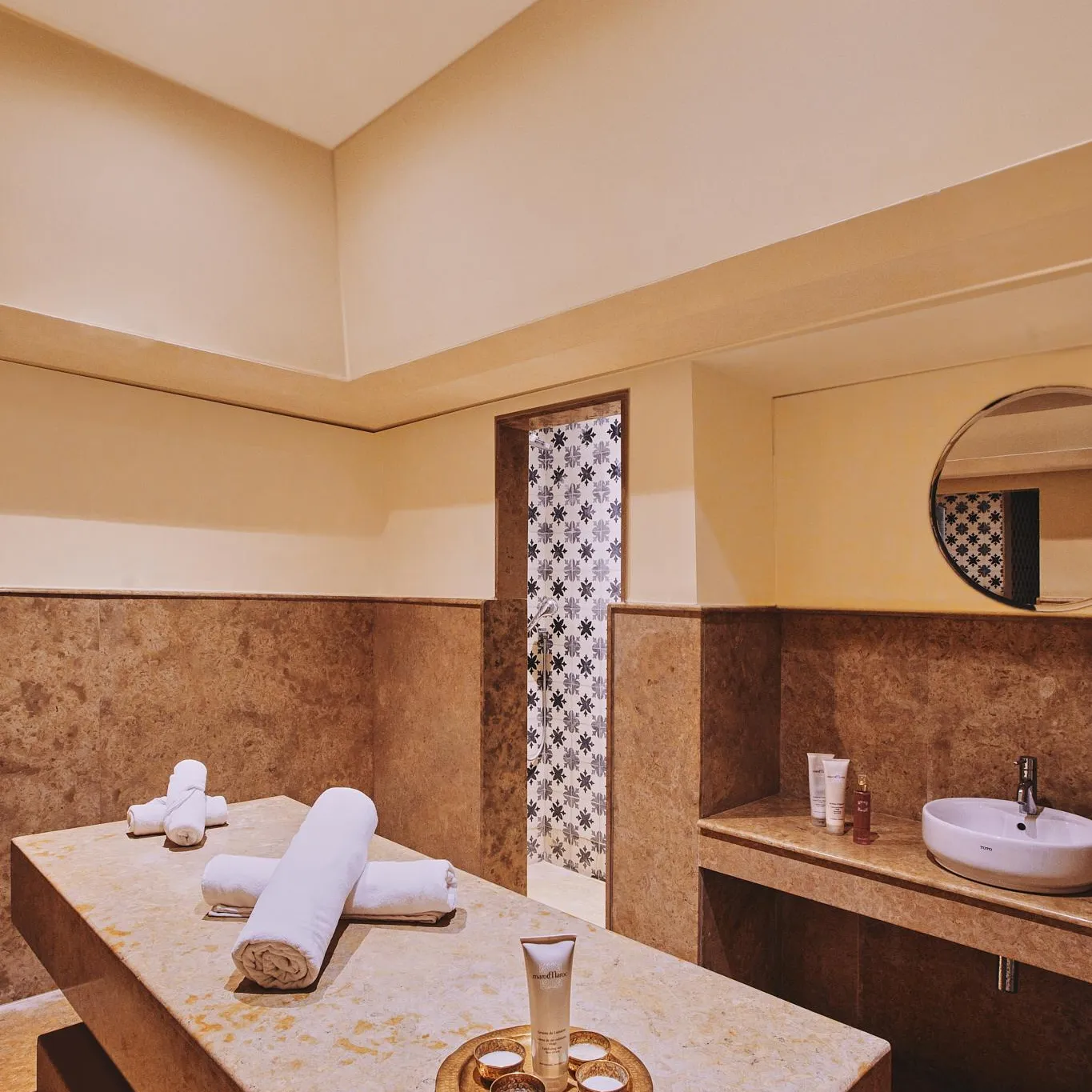 Salle de massage avec table de soins, serviettes, produits et lavabo dans un cadre aux murs en pierre et éclairage tamisé