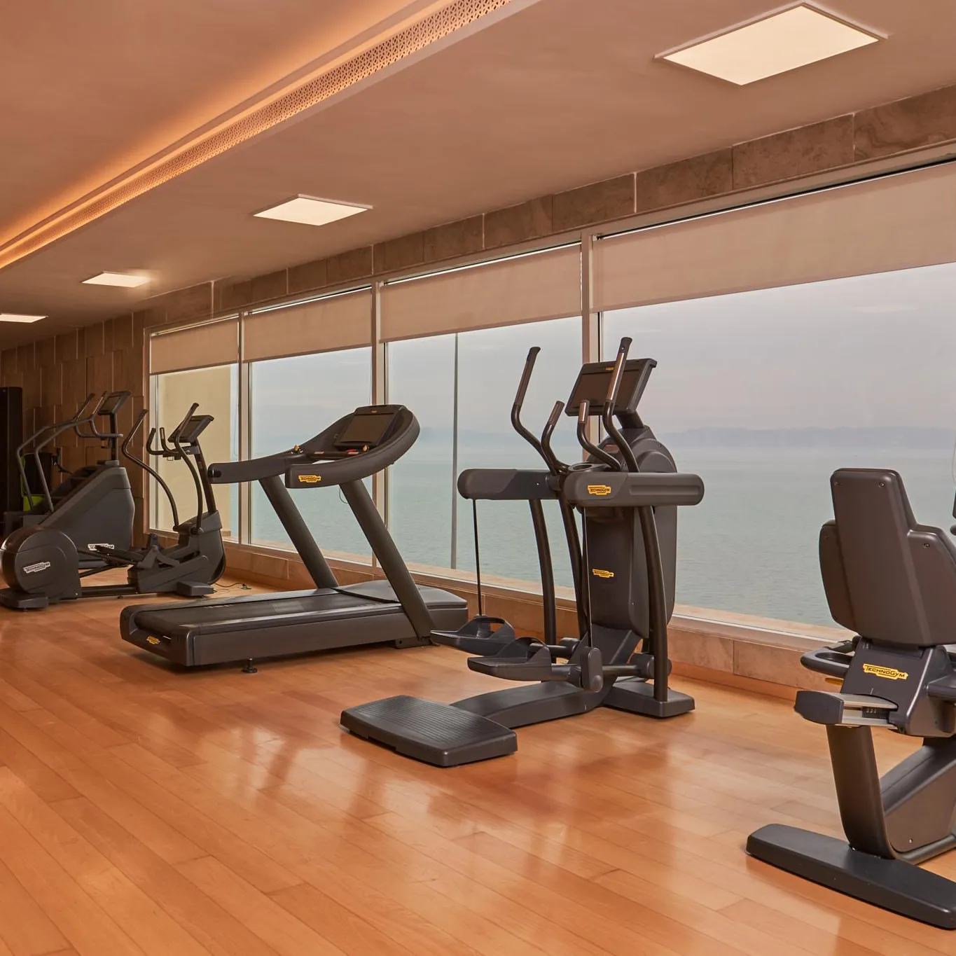 Salle de sport avec plusieurs appareils de fitness devant une grande fenêtre offrant une vue sur la mer