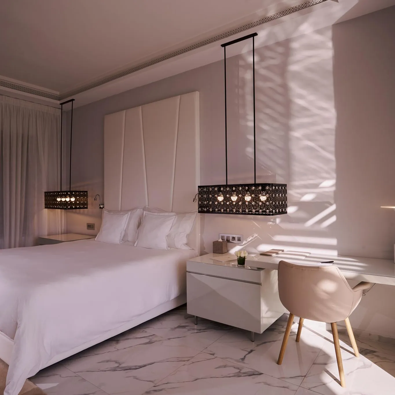 Chambre avec un lit double blanc, une table de chevet et une chaise près d'une fenêtre aux rideaux translucides