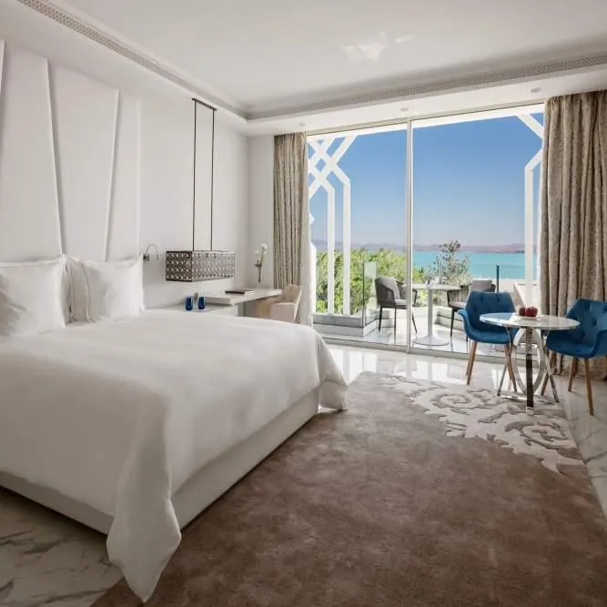 Chambre d'hôtel avec lit double, table et chaises près d'une grande baie vitrée offrant une vue sur la mer