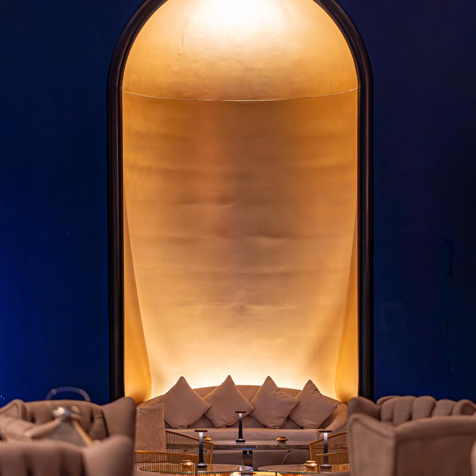 Un espace intérieur avec des canapés et une table basse, éclairé par une lumière dorée à travers une arche.