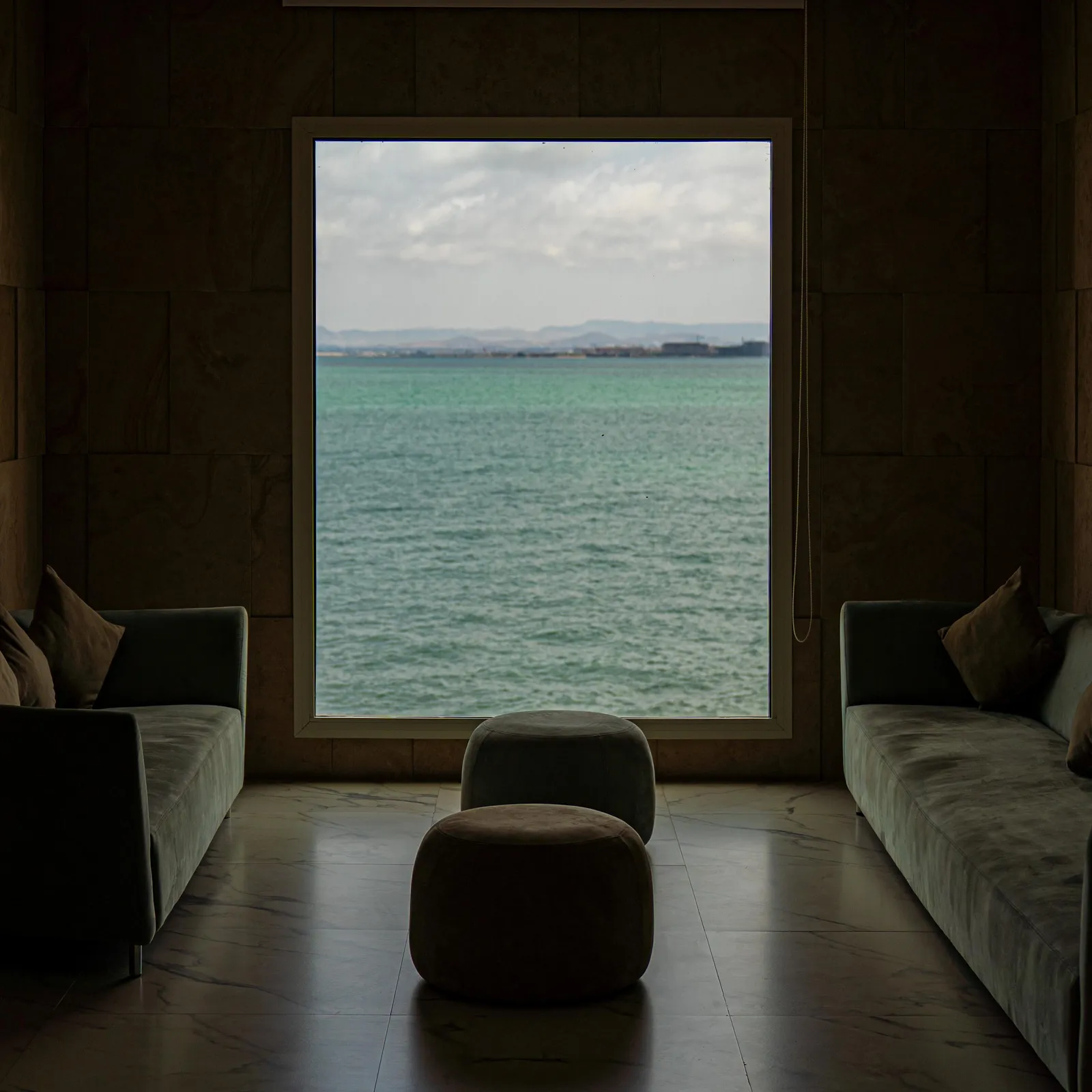 Pièce intérieure avec vue sur la mer à travers une grande fenêtre, meublée de deux canapés et d'un pouf