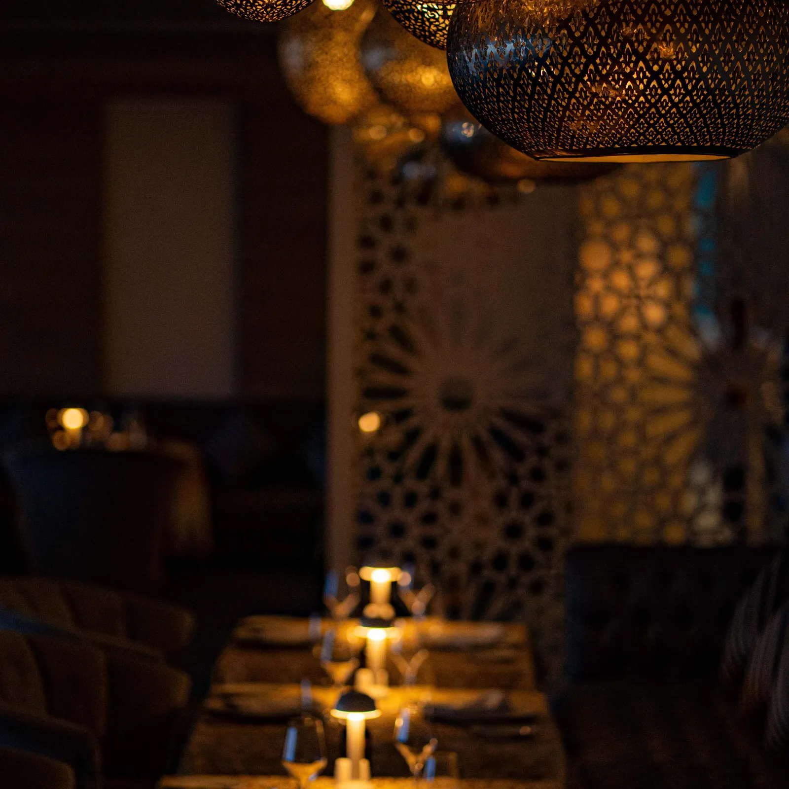 Une table dressée avec des verres, des bougies et des couverts sous des suspensions lumineuses dans un restaurant sombre
