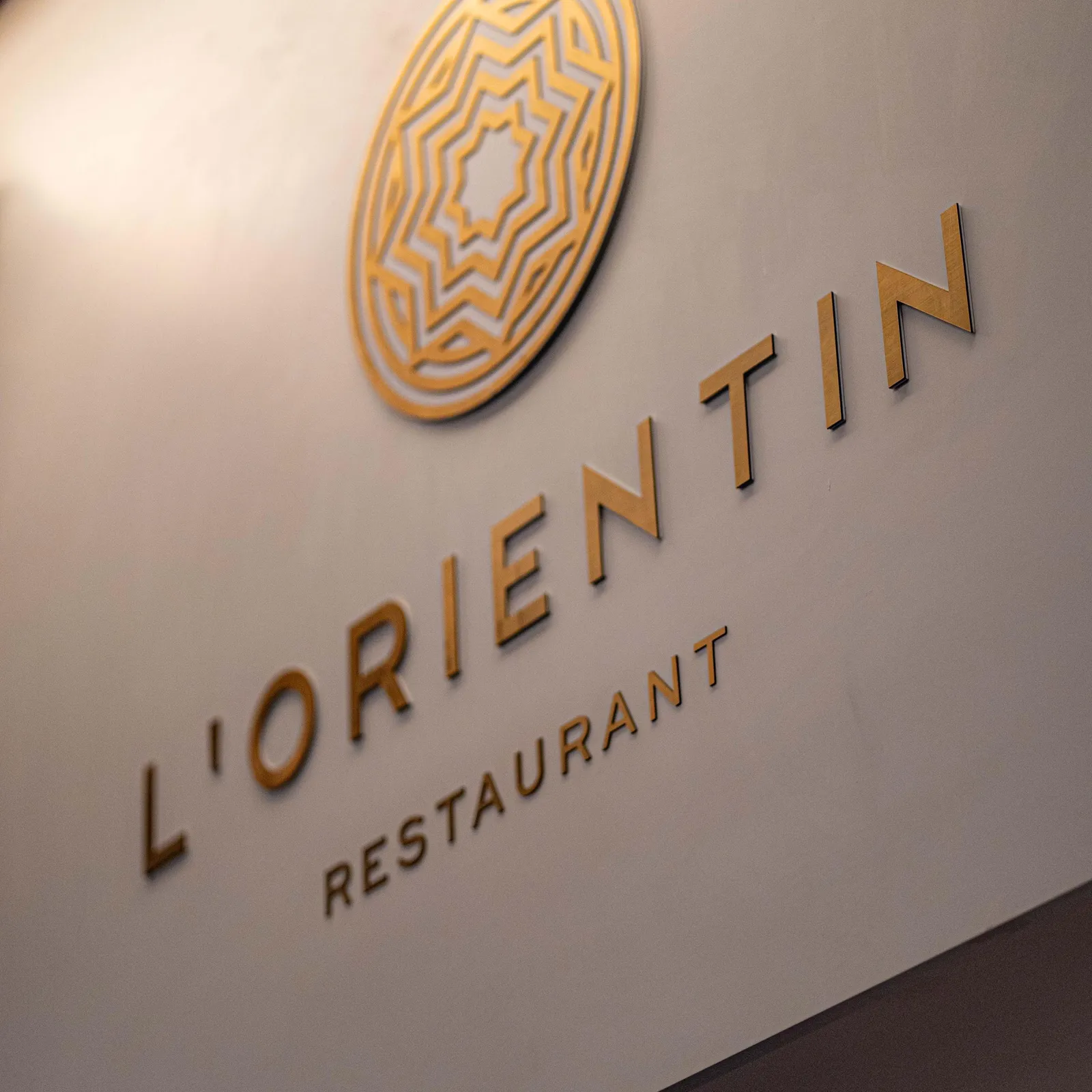 Plaque murale avec le logo et le nom "L'ORIENTIN RESTAURANT" en lettres dorées