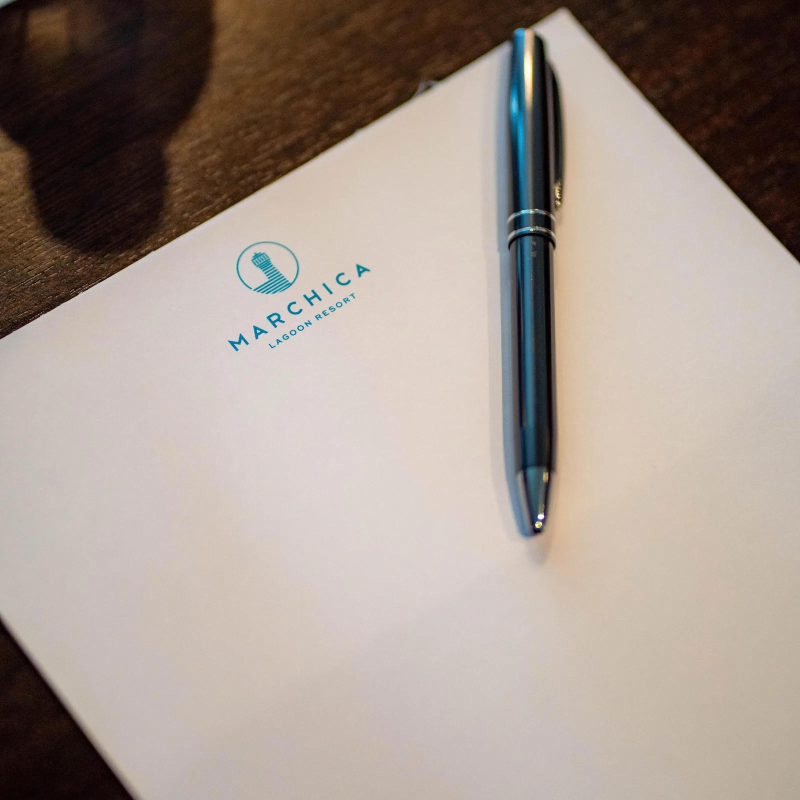 Une feuille de papier avec le logo "Marchica Lagoon Resort" et un stylo posé dessus sur une table en bois