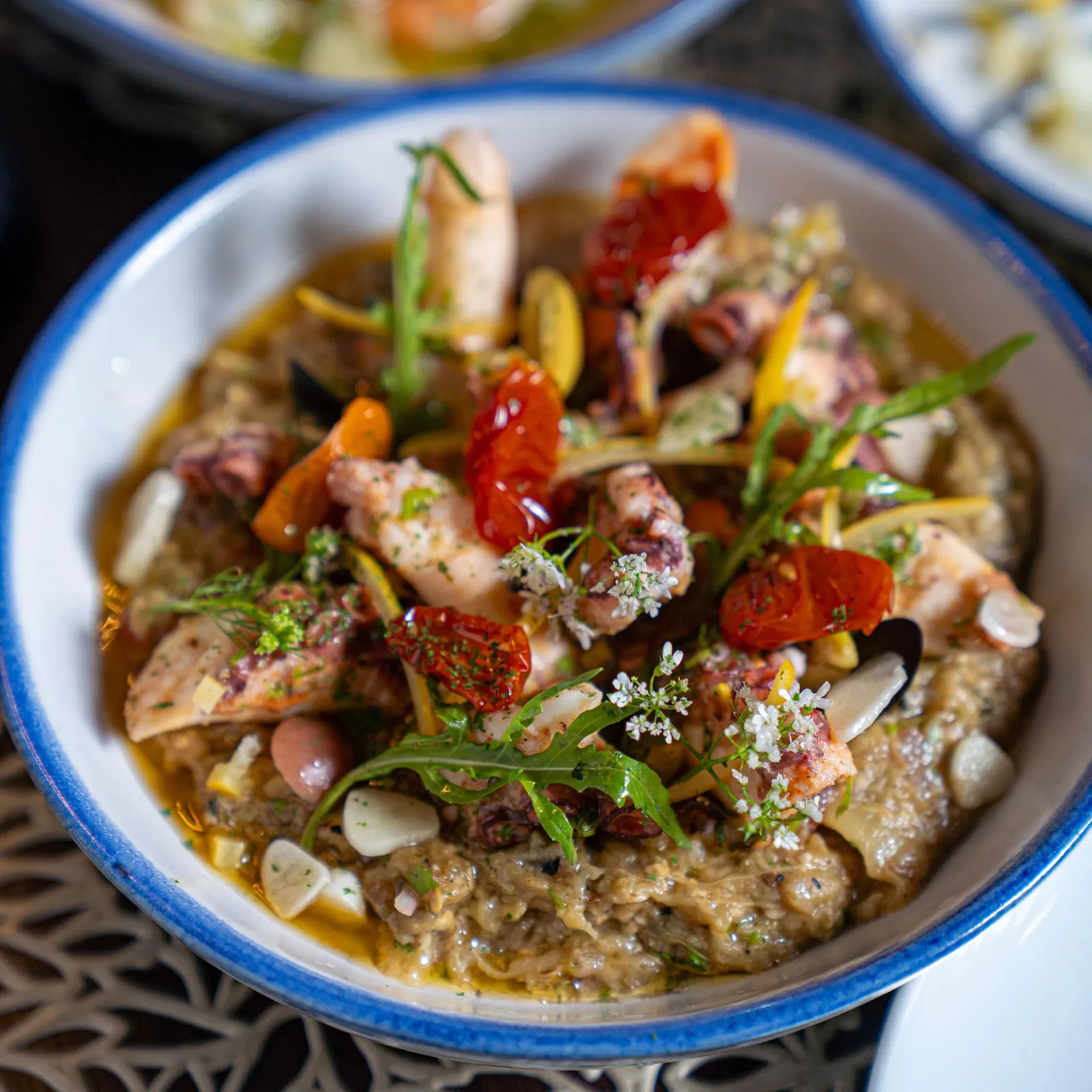 Bowl containing a dish with chickpeas, mushrooms, tomatoes, herbs, and spices, placed on a decorative metal tray