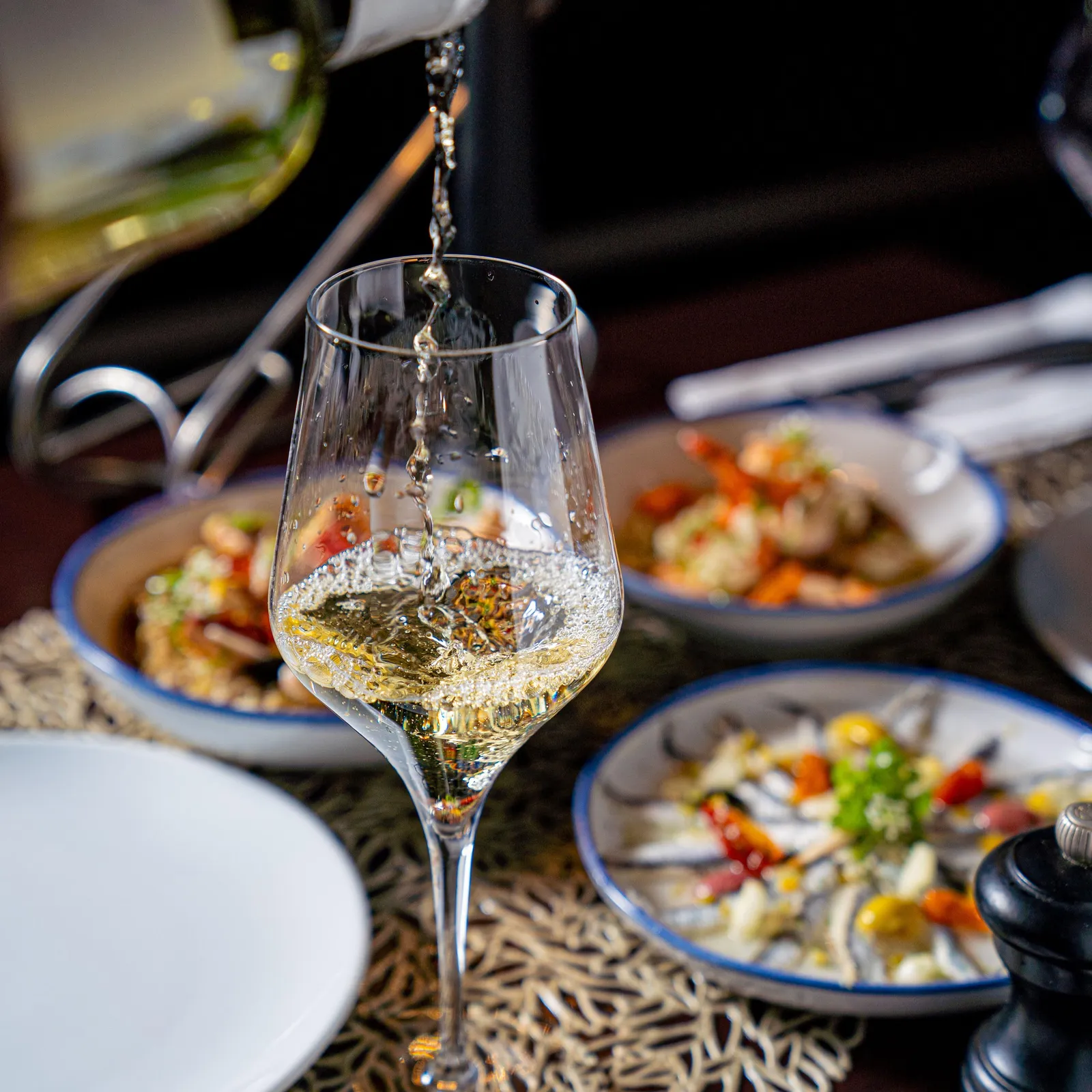Un verre à vin est rempli de vin blanc, avec des plats de salade et des couverts sur une table
