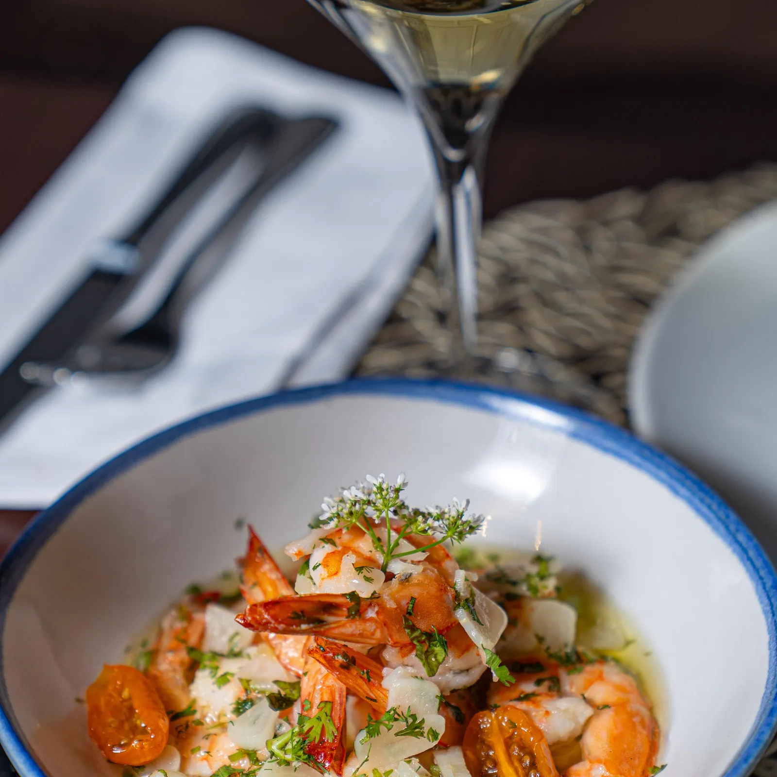 Un bol de crevettes grillées avec des tomates cerises et des oignons, accompagné d'un verre de vin blanc