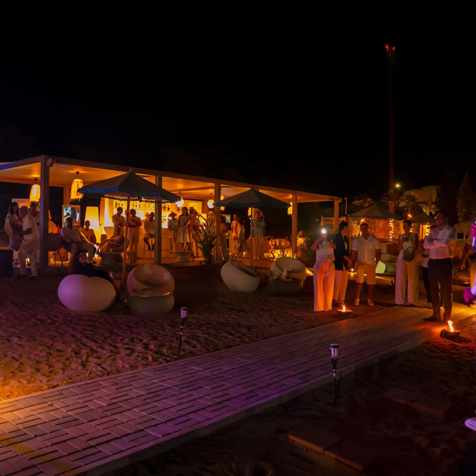 Un groupe de personnes se tient autour d'une structure éclairée sur une plage de nuit