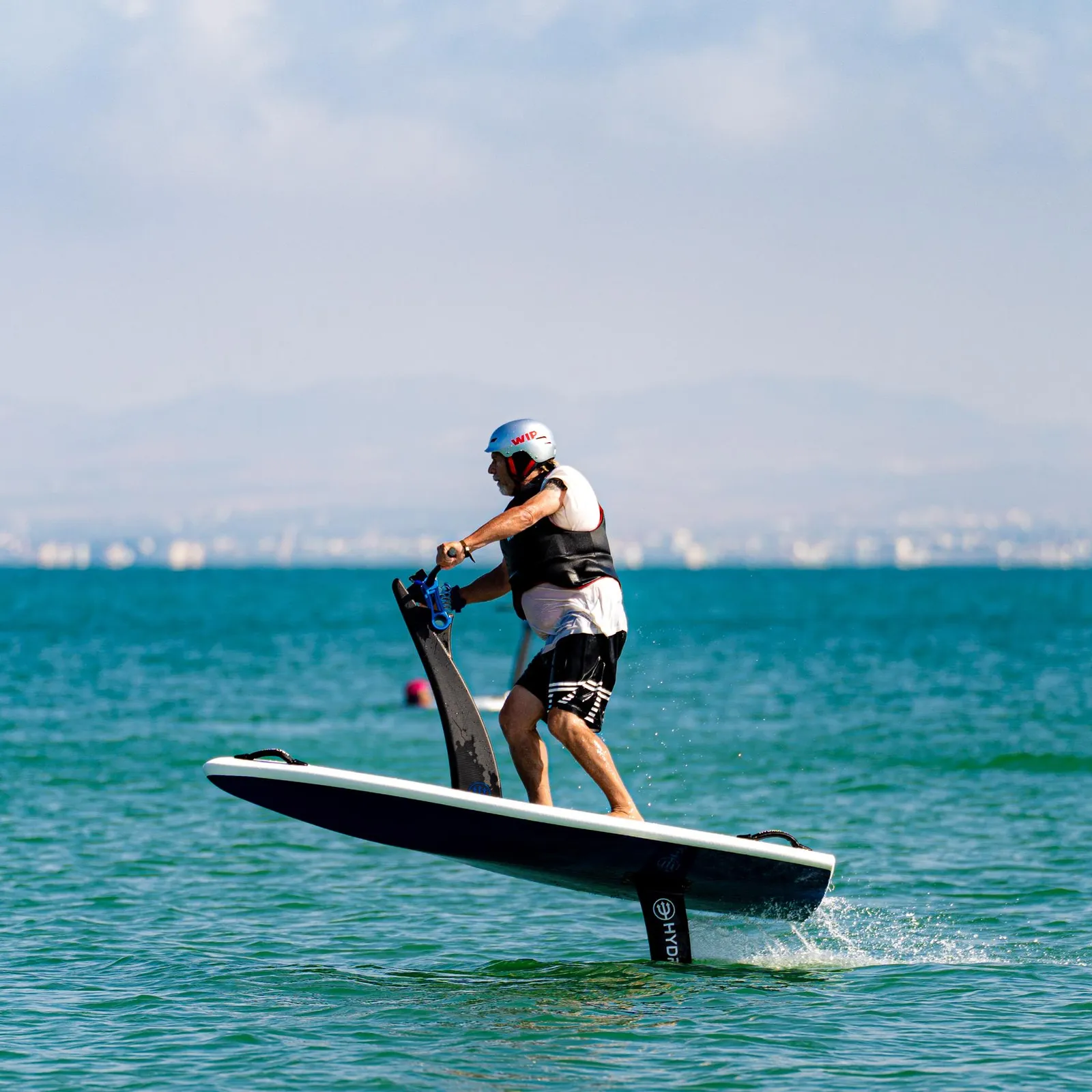 Une personne en combinaison et casque fait du hydrofoil sur une planche dans la mer