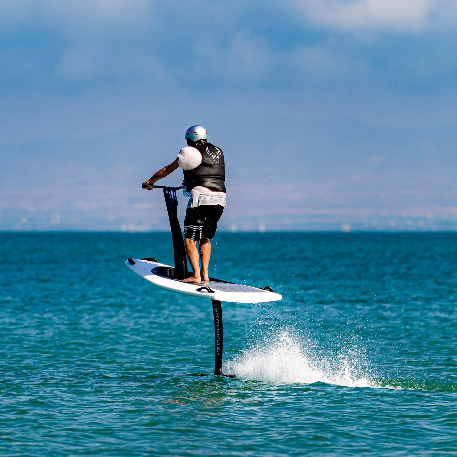 Un homme sur une planche de paddle électrique avance sur l'eau avec un jet d'eau derrière lui