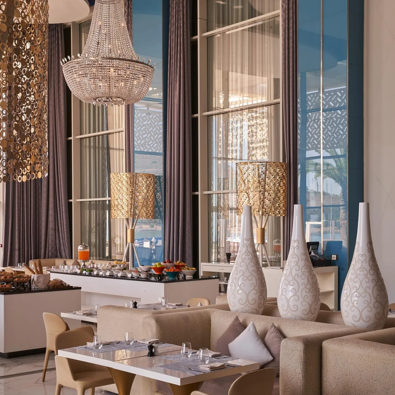Salle à manger élégante avec tables, chaises, canapés, lustres et vue sur la mer à travers de grandes fenêtres