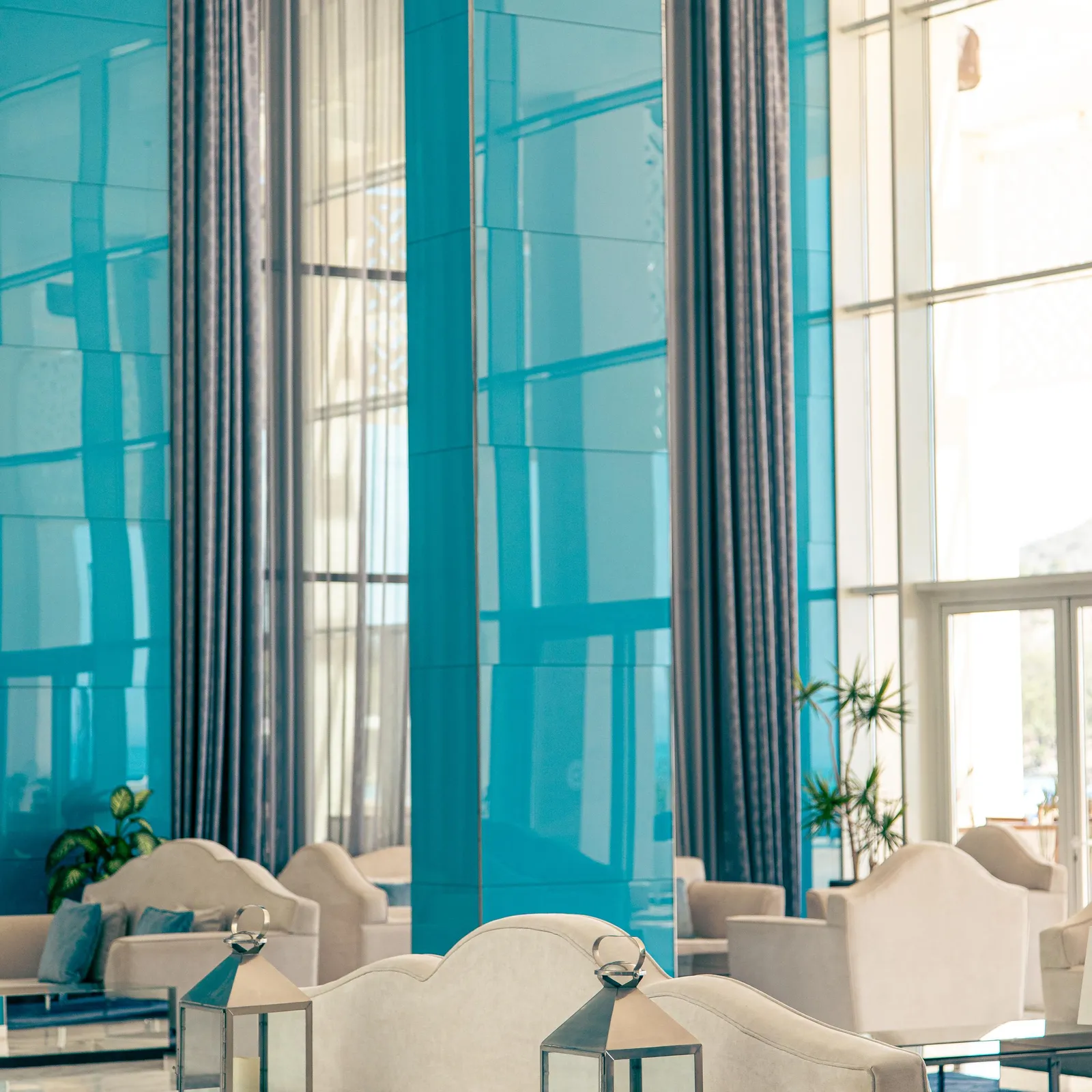 Un salon moderne avec des canapés blancs, des lanternes sur une table basse et de grandes fenêtres bleues