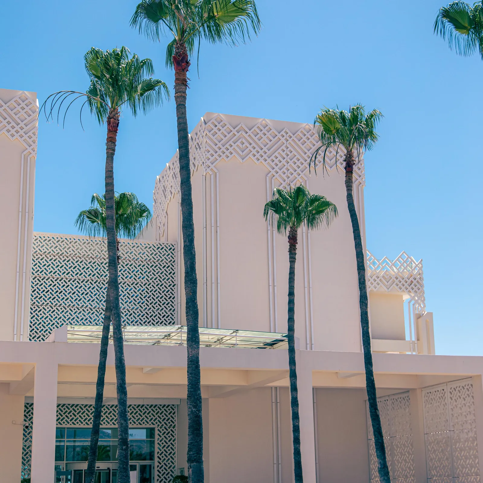 Un bâtiment beige avec des motifs géométriques et des palmiers devant une fontaine
