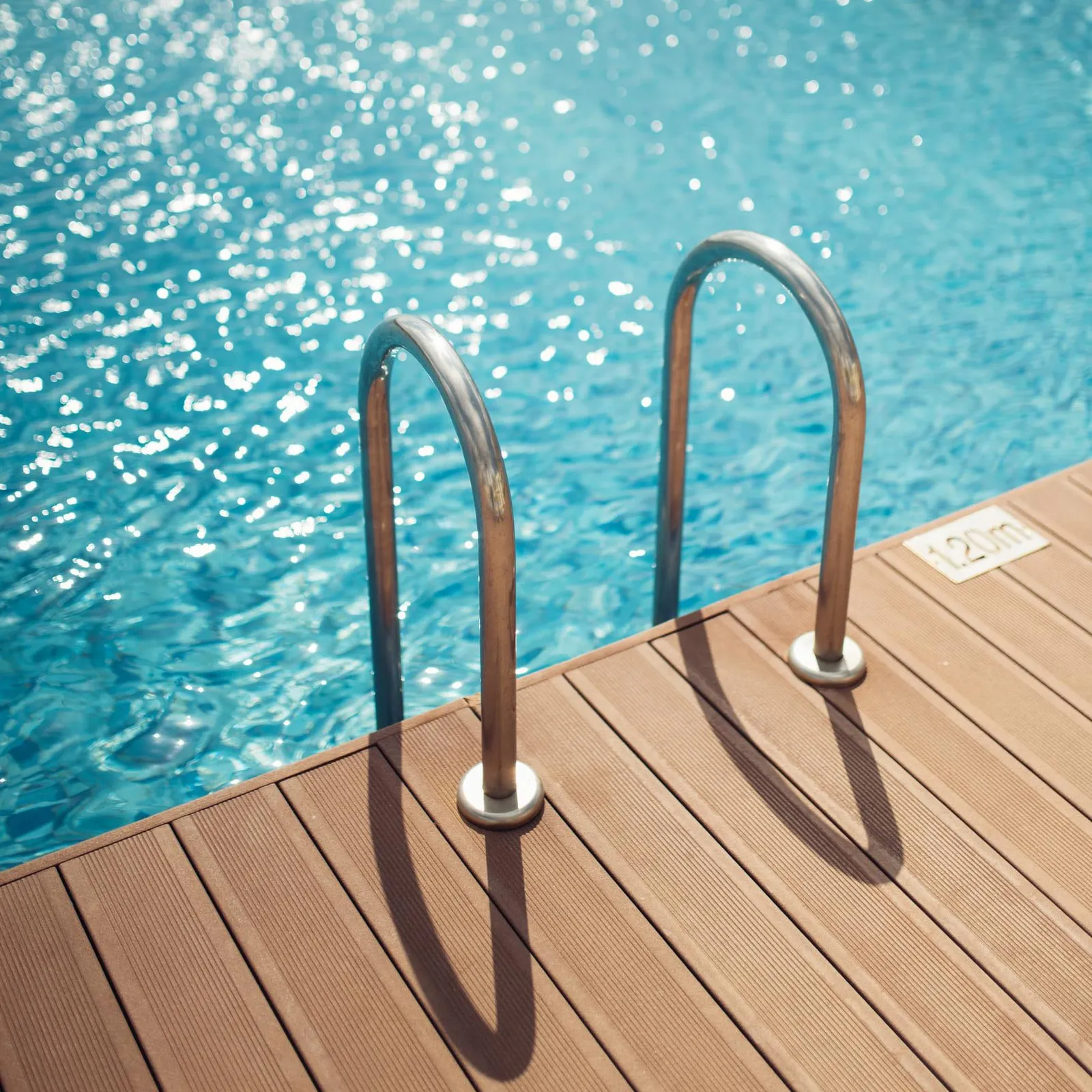 Deux barres métalliques courbées fixées sur un plancher en bois près d'une piscine remplie d'eau bleue