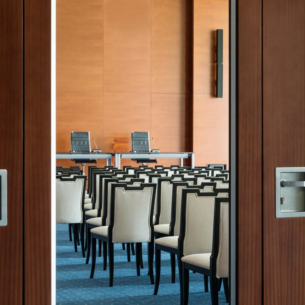 Vue d'une salle de conférence à travers une porte en bois avec des rangées de chaises alignées et deux sièges à une table au fond