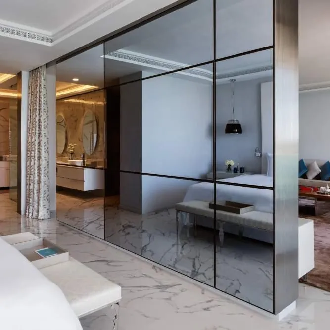 Intérieur moderne avec un miroir séparant une chambre à coucher et un salon, montrant des meubles blancs et un coin salon avec canapé et fauteuil