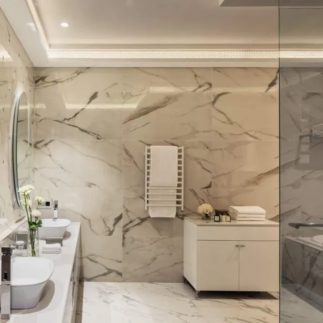 Salle de bain moderne avec double vasque, miroir rond, douche vitrée et murs en marbre beige