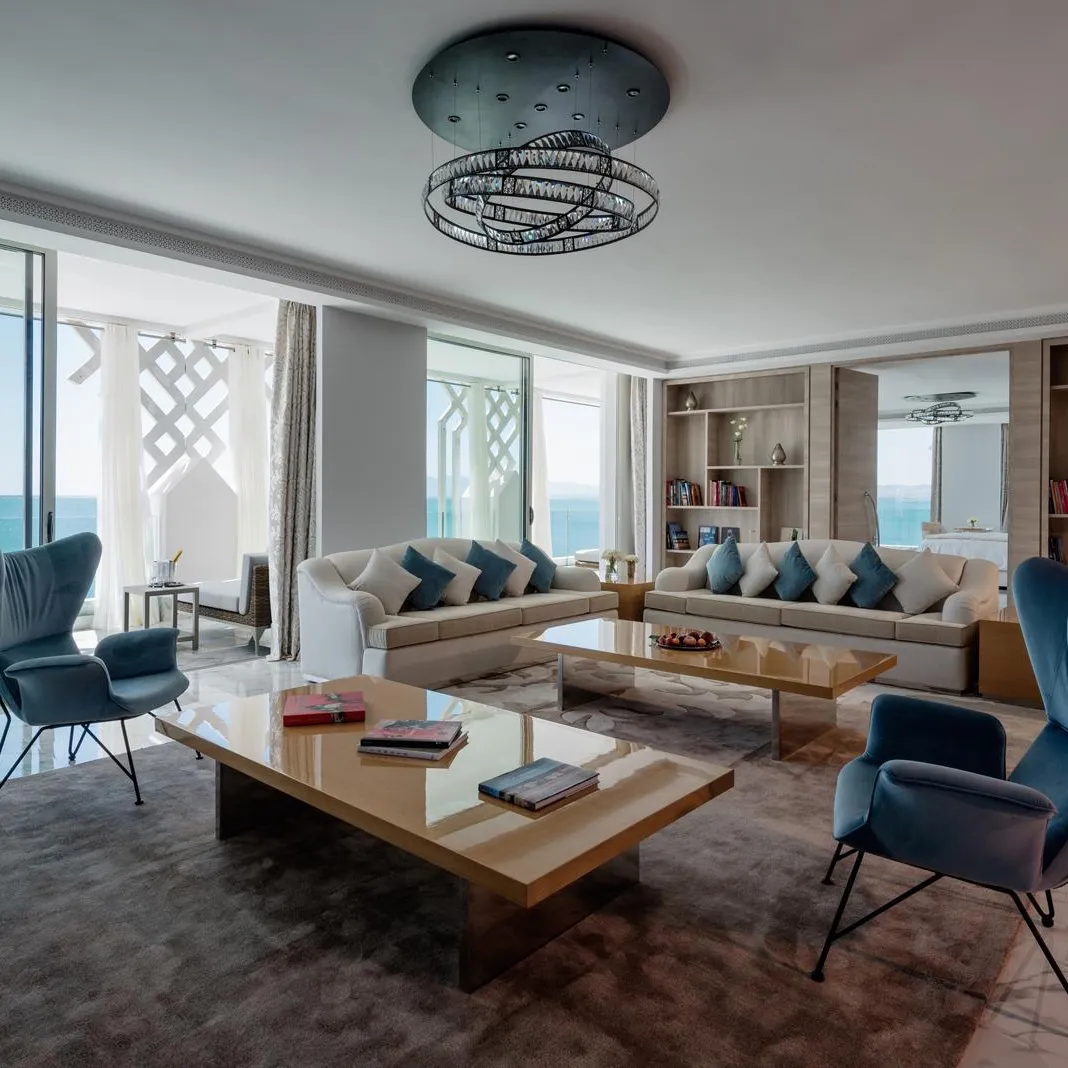 Salon moderne avec vue sur la mer, comprenant un canapé, des fauteuils, une table basse et des étagères remplies de livres