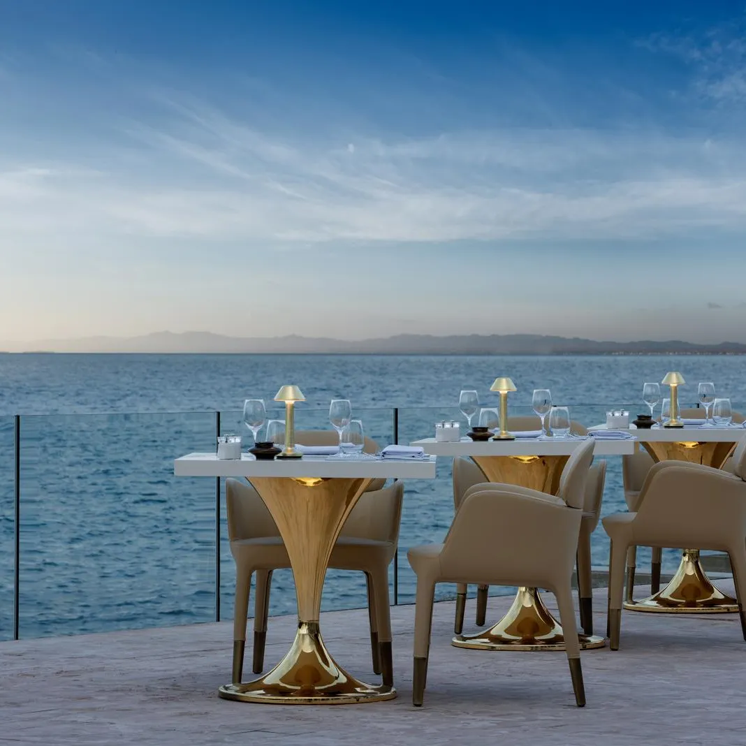 Tables et chaises disposées sur une terrasse face à la mer avec des verres et des serviettes, sous un ciel dégagé