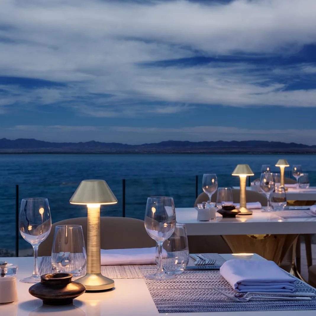 Tables dressées avec verres et bougies sur une terrasse face à la mer au coucher du soleil