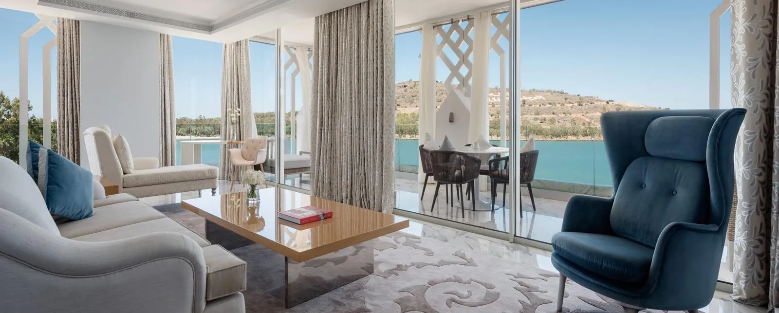Salón moderno con sofá, sillón y mesa de centro, con acceso a una terraza con vistas a una piscina y colinas