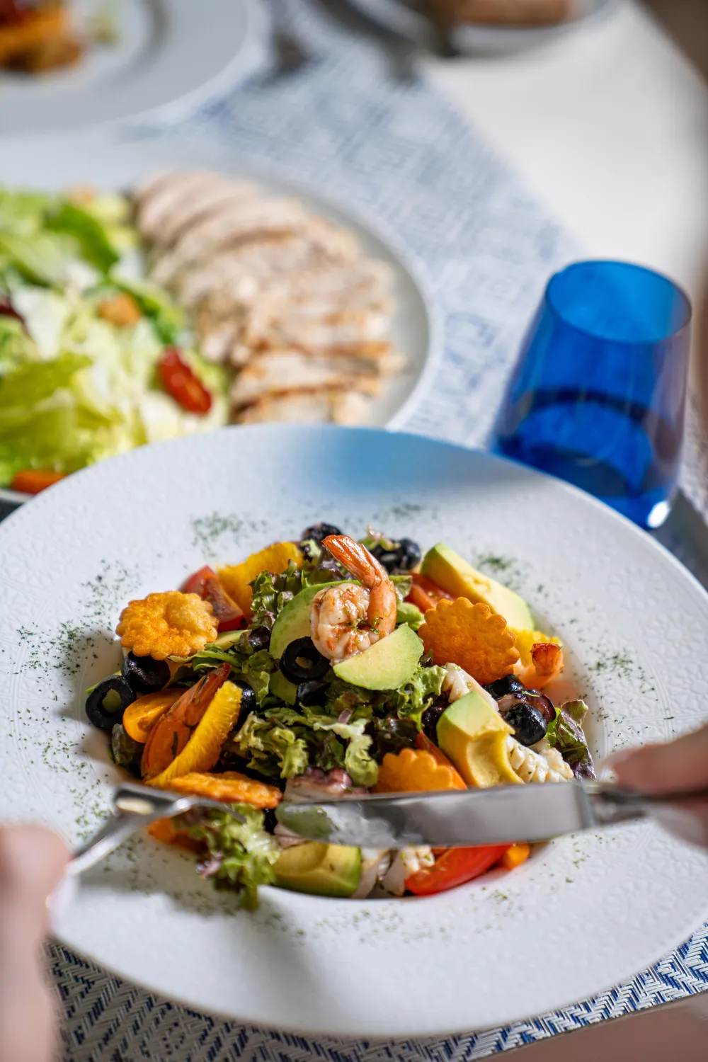 Une assiette de salade composée avec des crevettes, des morceaux d'avocat, des olives, des légumes et des croûtons, accompagnée d'une fourchette