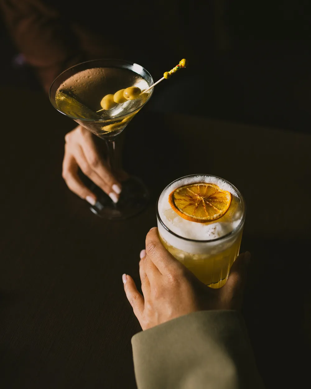 Deux mains tiennent des verres contenant des boissons, l'un avec des olives et l'autre avec une tranche de citron