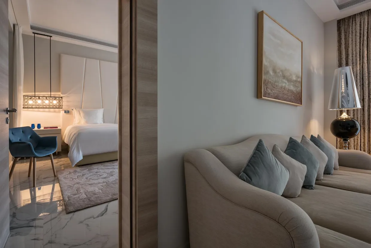 Modern hotel room with bed, sofa, desk, and bedside lamp