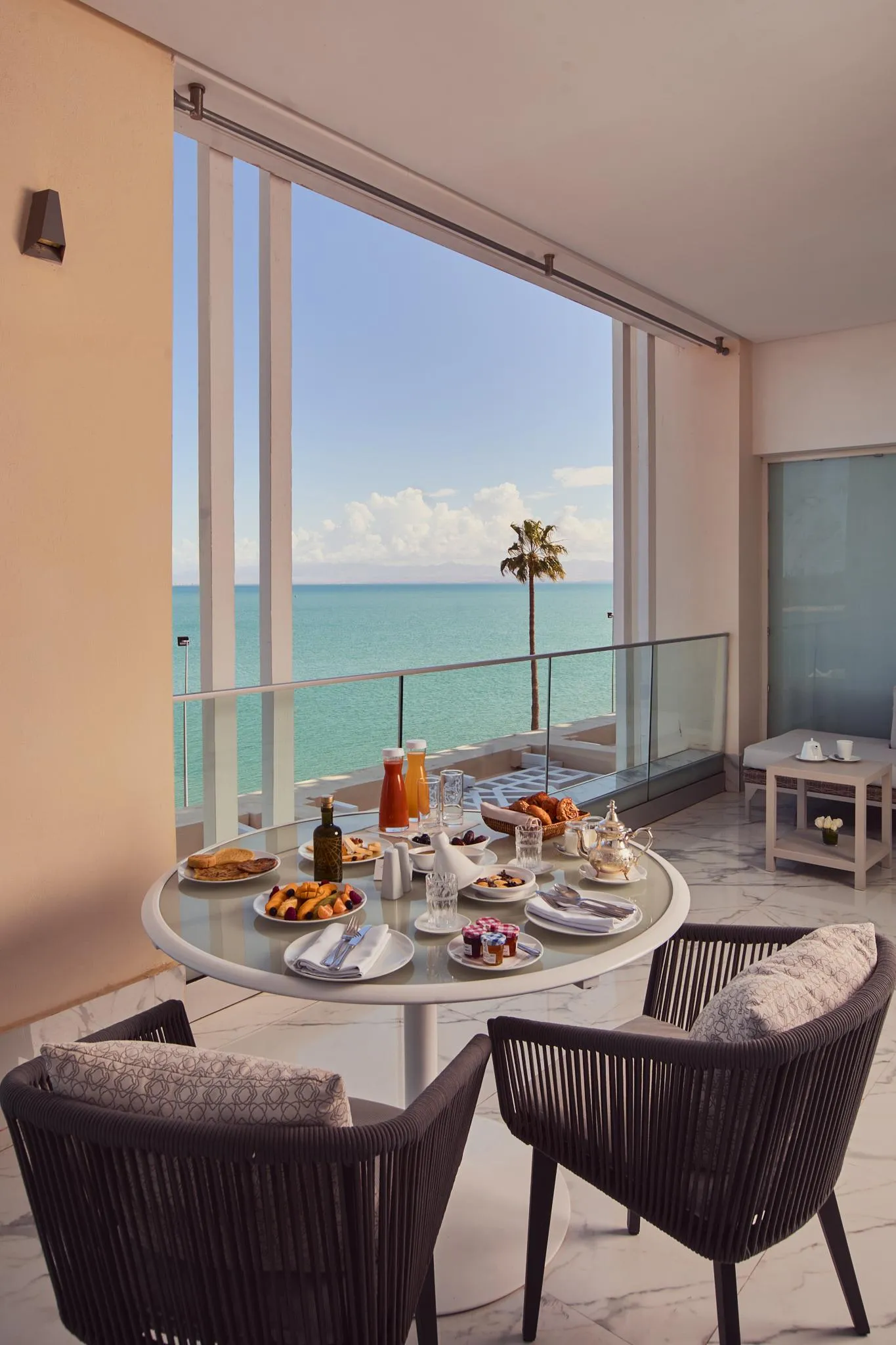 Mesa redonda con desayuno en un balcón frente al mar, vista al océano y una palmera