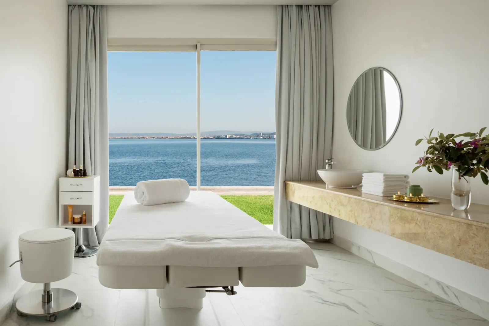 Salle de massage avec table de soins, vue sur la mer, lavabo et miroir rond