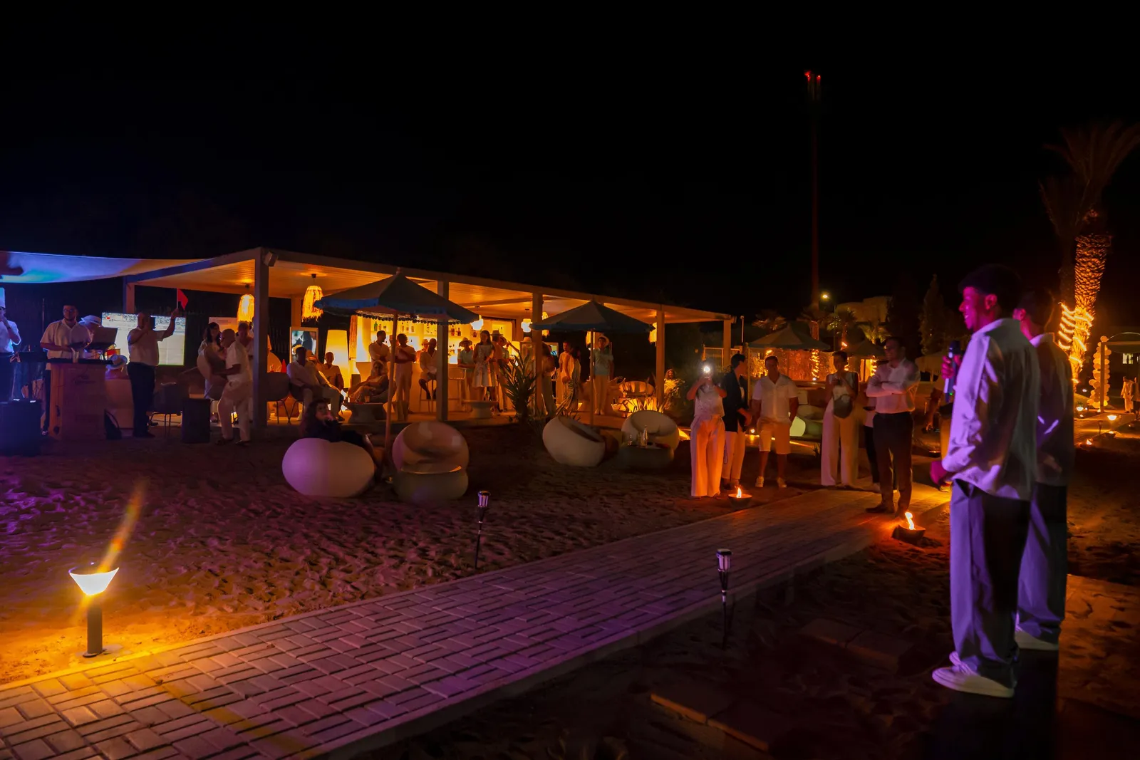 Un groupe de personnes se tient autour d'une structure éclairée sur une plage de nuit