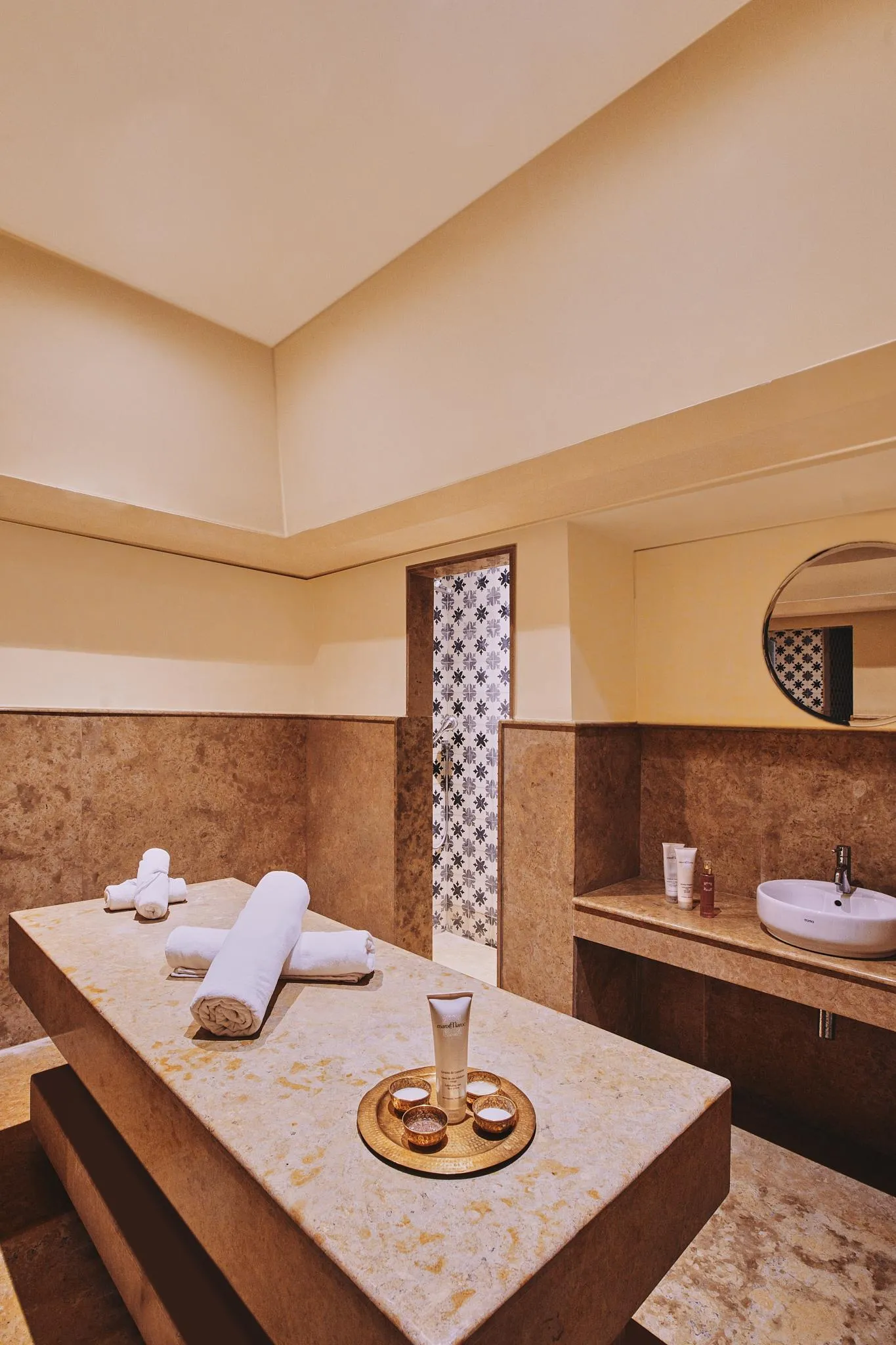 Massage room with treatment table, towels, products, and sink in a setting with stone walls and dim lighting.