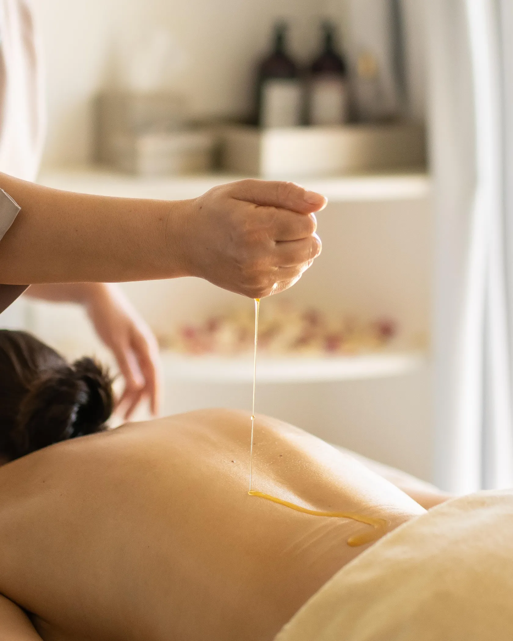 A person pours a liquid onto the back of a person lying on a massage table.