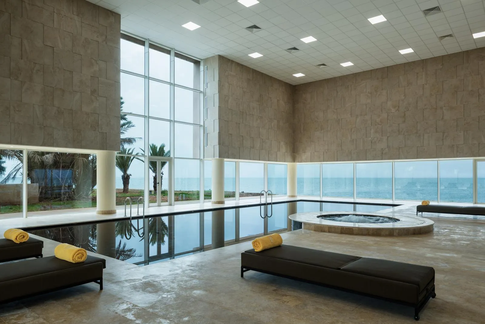 Piscina interior con vista al mar, rodeada de sofás y toallas amarillas