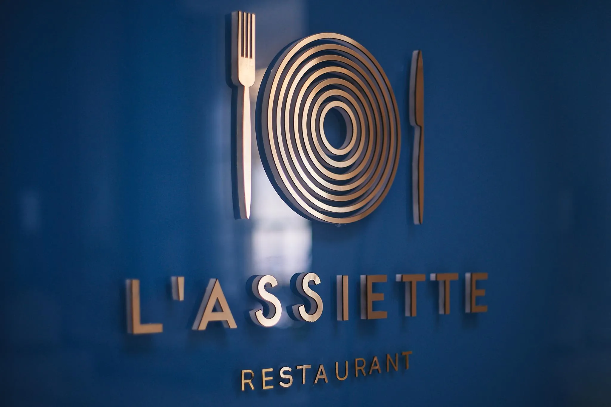 Wall plaque of a restaurant named "L'Assiette" with a logo depicting a plate between two cutlery items