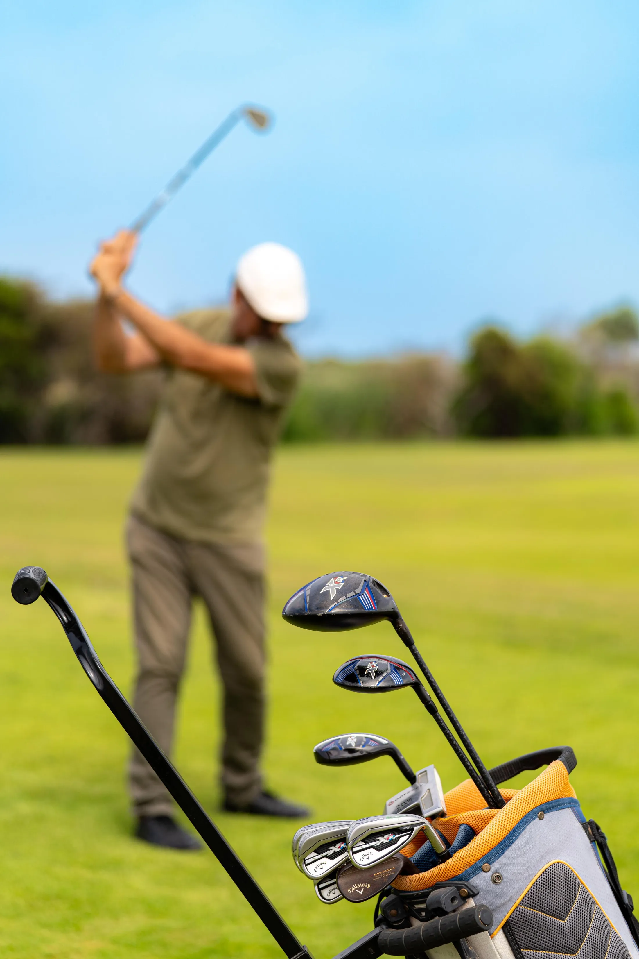 A golfer in action on a green with a bag of clubs nearby