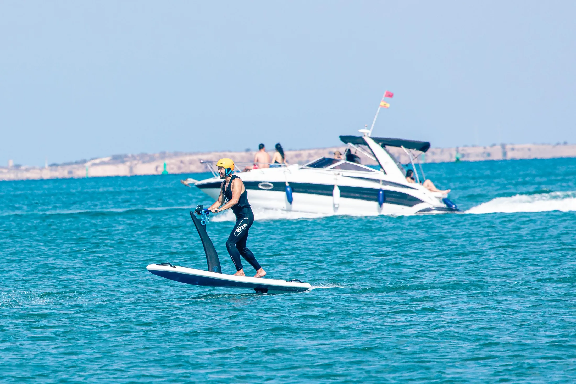 A person is paddleboarding with a paddle in the sea, a boat is visible in the background.