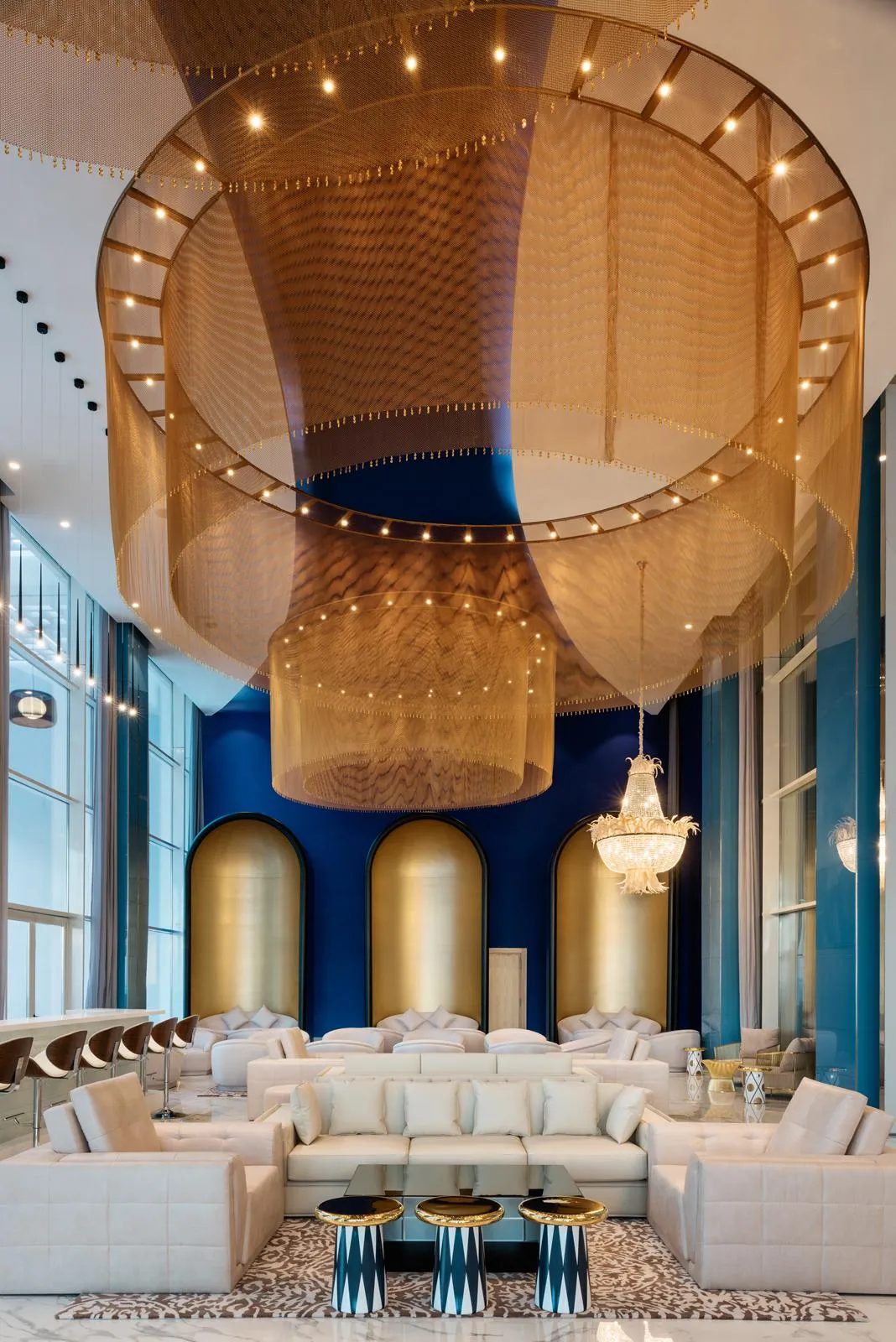 A luxurious lounge with white sofas, coffee tables, and a ceiling decorated with golden fabrics and lights.