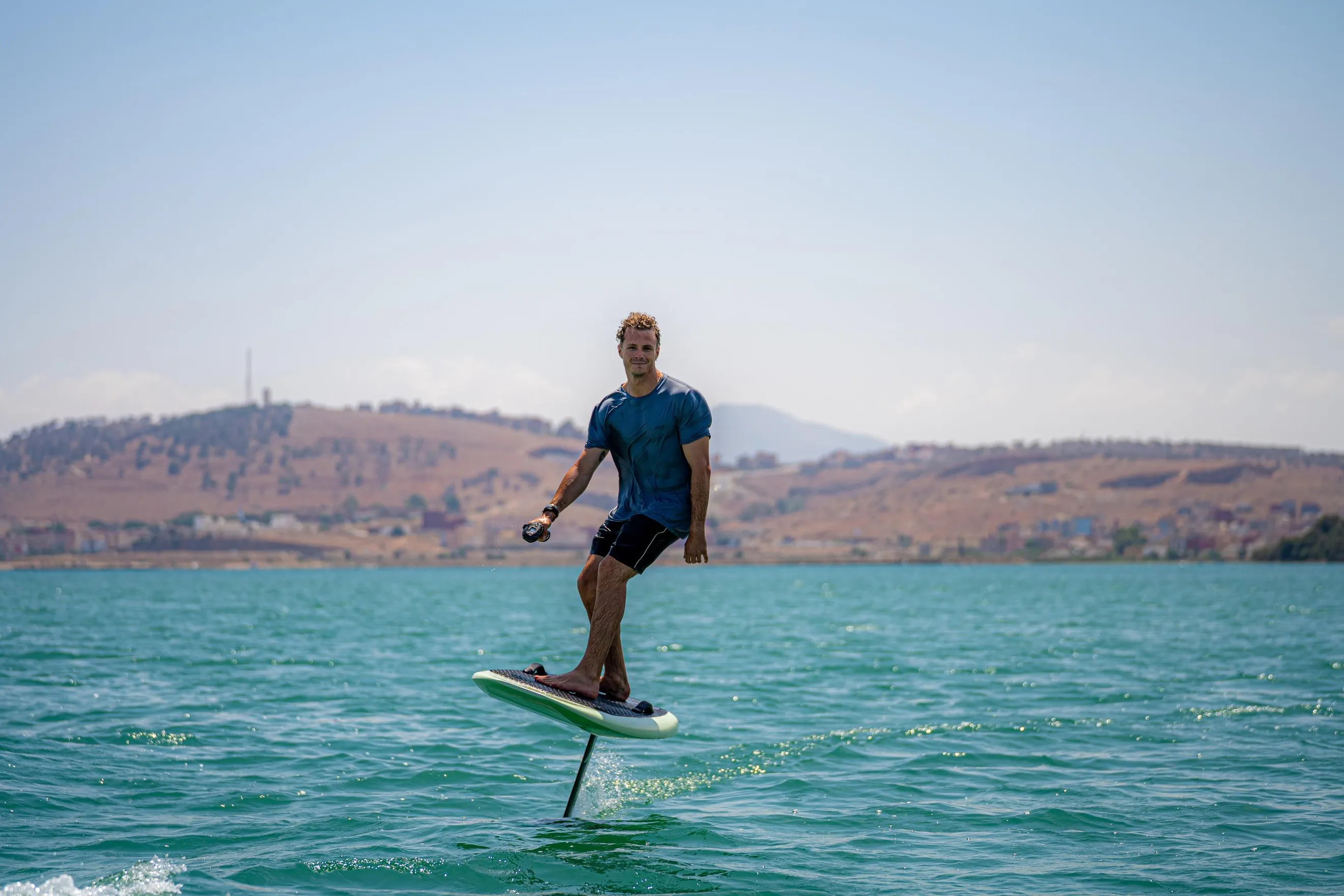 Un hombre de pie sobre una tabla de paddle en una extensión de agua con colinas de fondo