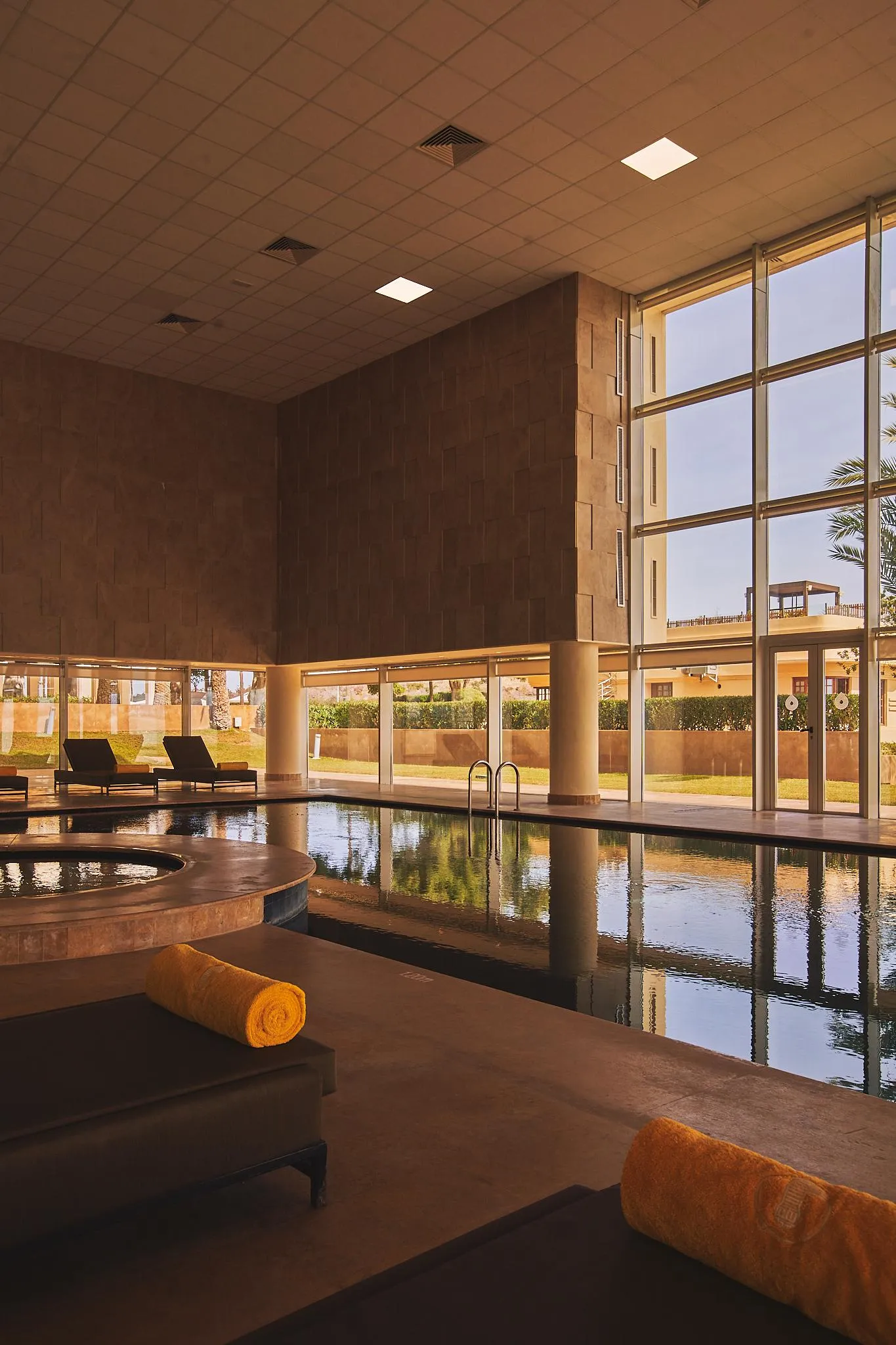 Indoor pool with sun loungers and towels, surrounded by large windows and stone walls